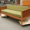 Mid-century modern sofa on dolly, light wood and olive green fabric.